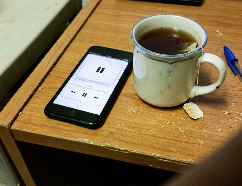 A smartphone playing a podcast next to a mug of tea on a desk, representing popular UK business podcasts.