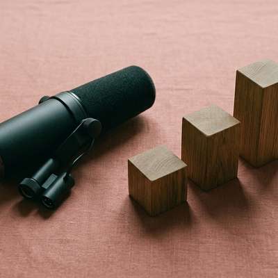 A studio microphone next to three wooden blocks of graduating heights, representing podcast growth and analytics.