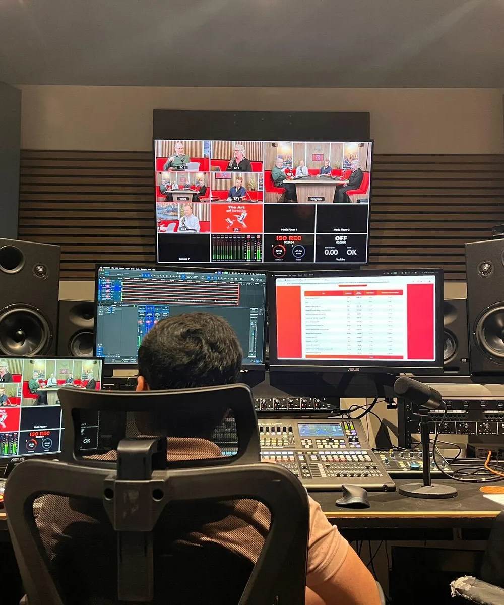 A corporate training video being filmed in a studio, with a presenter on camera and a monitor showing the editing timeline behind the crew.