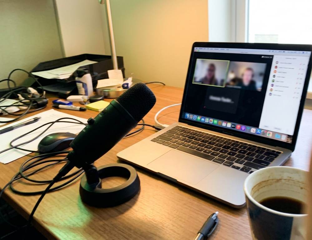 A USB microphone and open laptop on an office desk, illustrating a B2B remote podcast guesting setup.