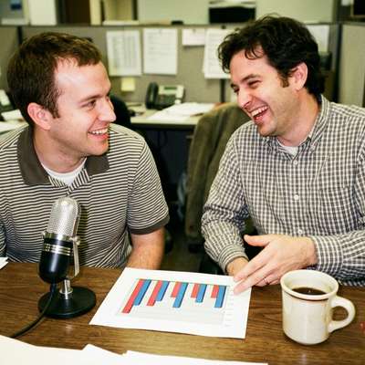 Two office colleagues analyze a printed performance chart next to a podcast microphone, representing B2B podcast metrics.